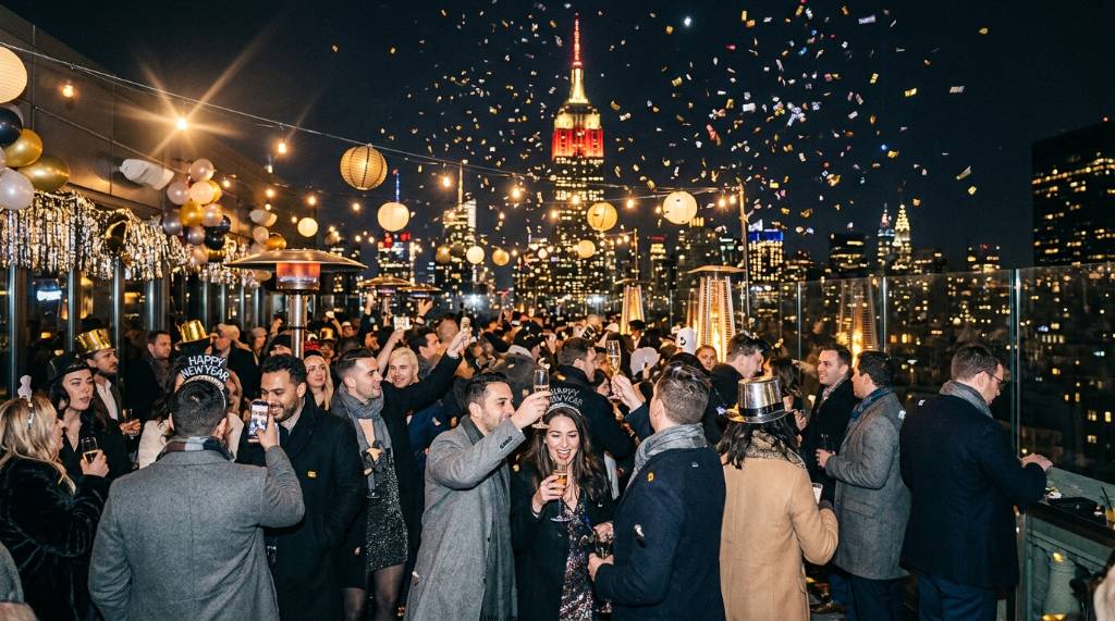 Crowded rooftop bar in Manhattan with guests celebrating New Year's Eve and the Empire State Building in the background