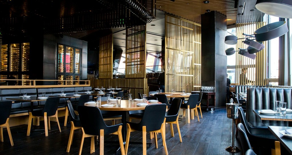 Outdoor heated restaurant patio overlooking Rockefeller Center ice skating rink with diners and Christmas tree view